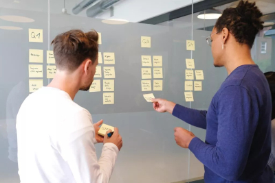 Two people stand before a glass wall adorned with colourful sticky notes, brainstorming ideas